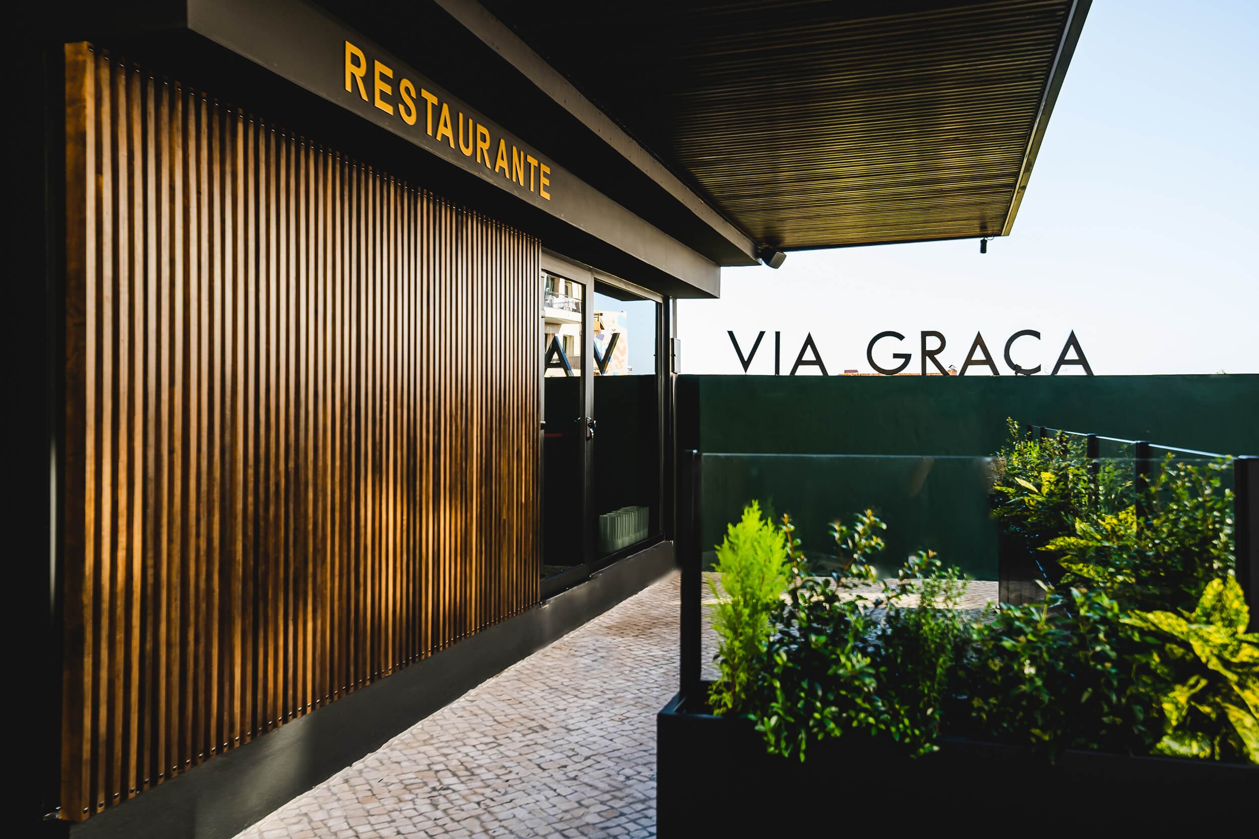 Entrance decorated with wood and green tones, with bold letters "Via Gracia"